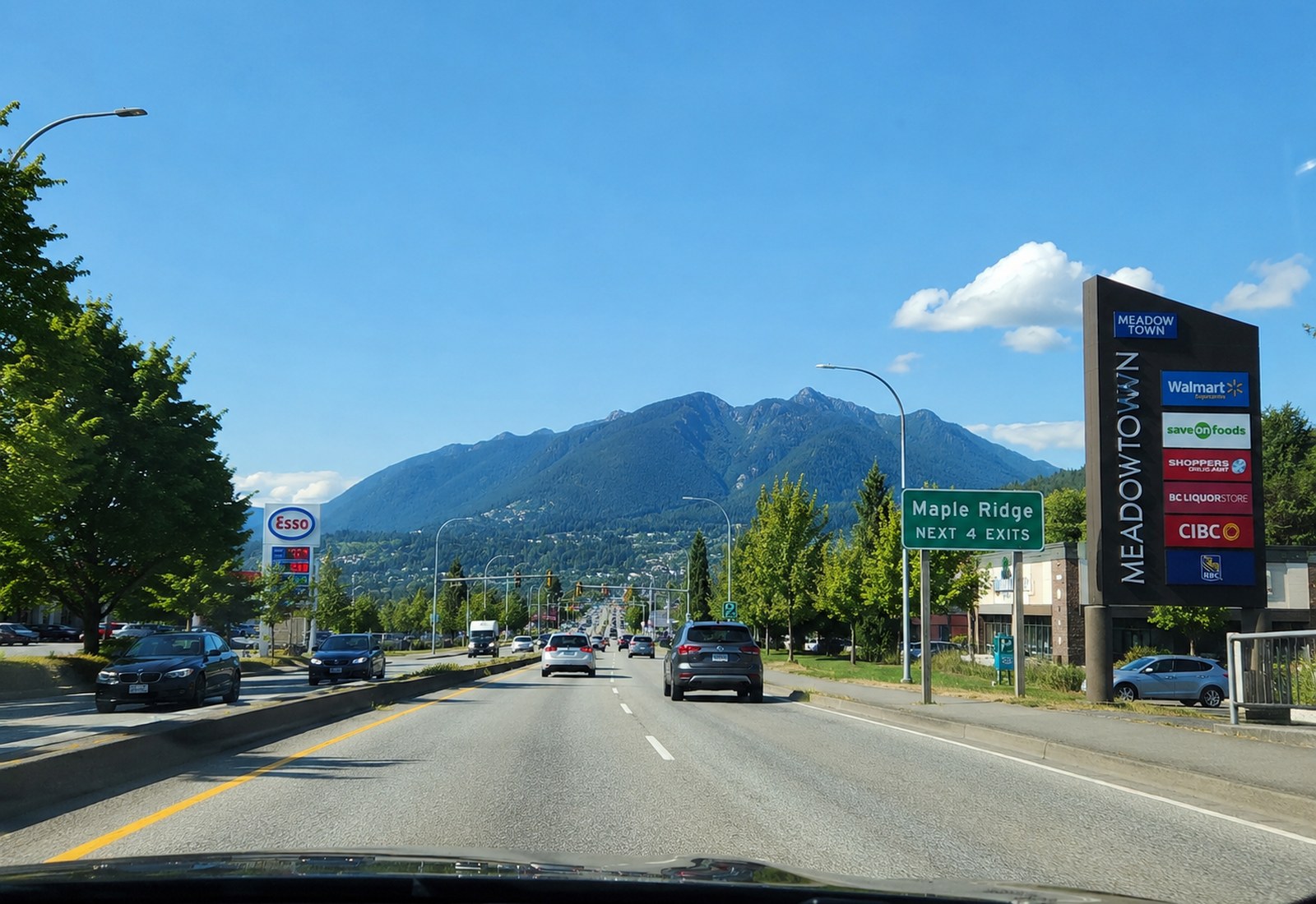 The view from a car on Lougheed Highway approaching Maple Ridge, with a Maple Ridge next-four-exits sign and the mountains ahead